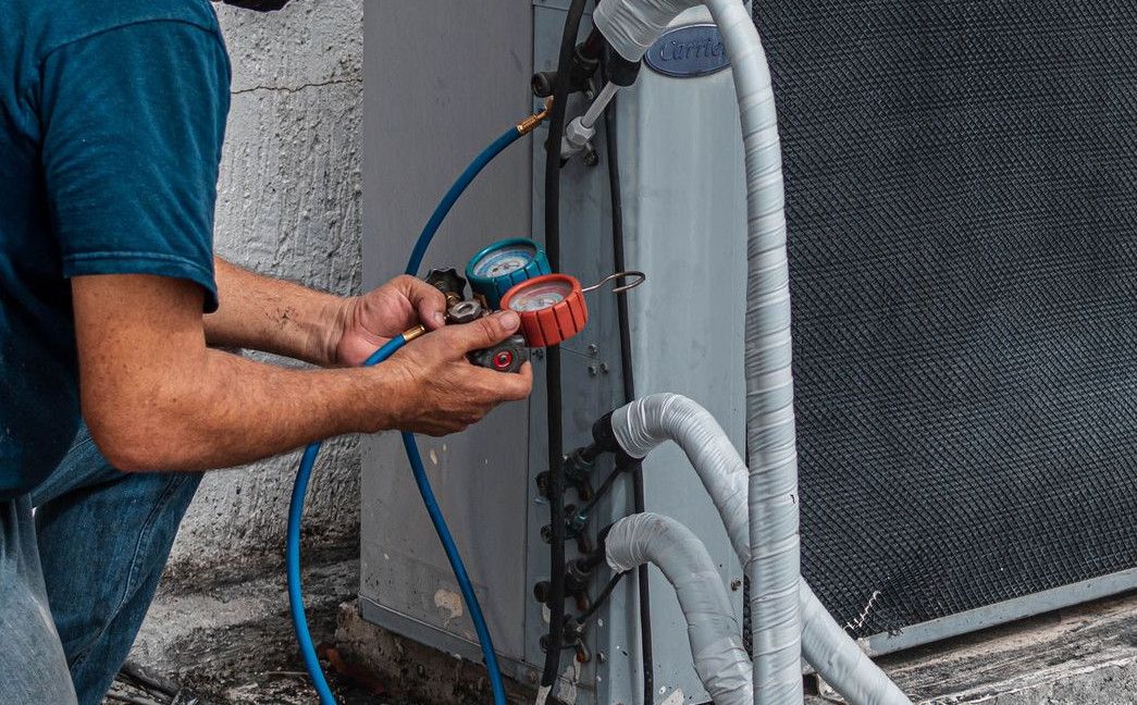 Technician repairing an air conditioner unit outdoors, wearing a facemask and using a manifold gauge.